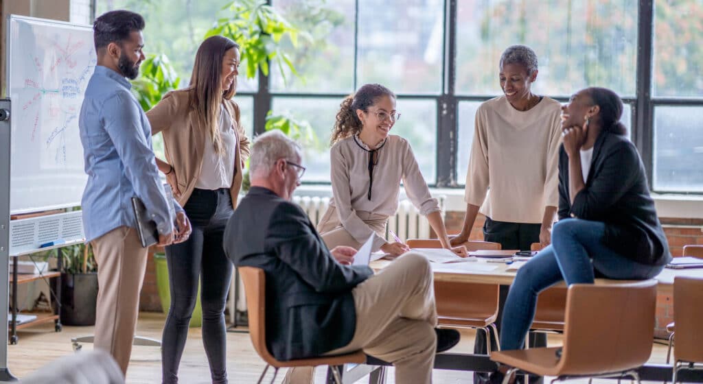 A diverse group of people having a meeting in a modern office with large windows and plants.