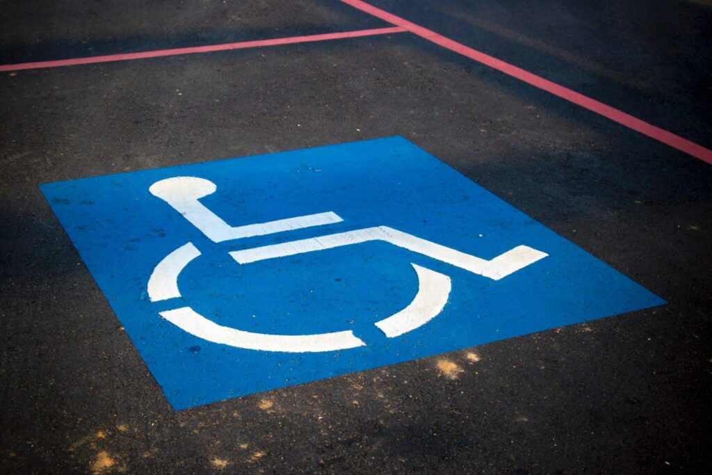 A blue parking space with a white wheelchair symbol on asphalt, marked by red lines.