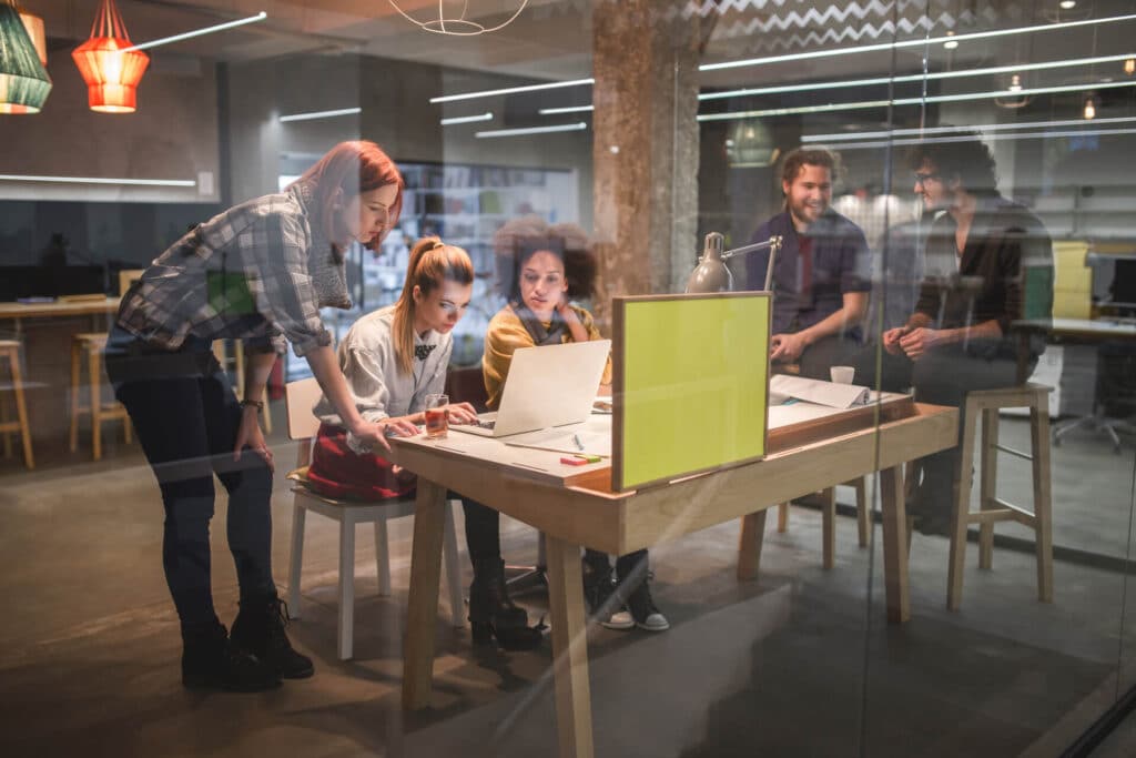 A group of people collaborating around a table with a laptop in a modern office setting.