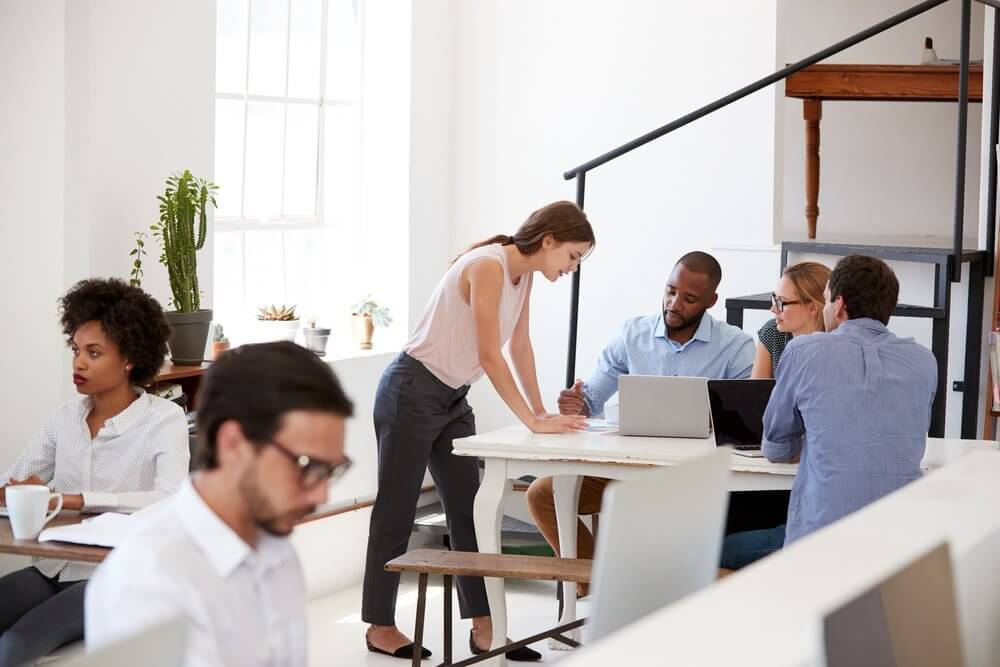 People working collaboratively around a table in a bright office space with natural light and laptops.