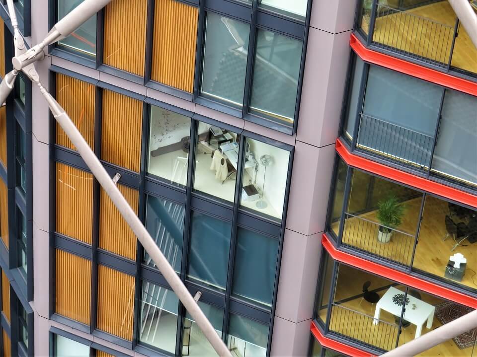 Close-up of a modern building with large windows, visible wooden panels, and interiors, including plants and furniture.