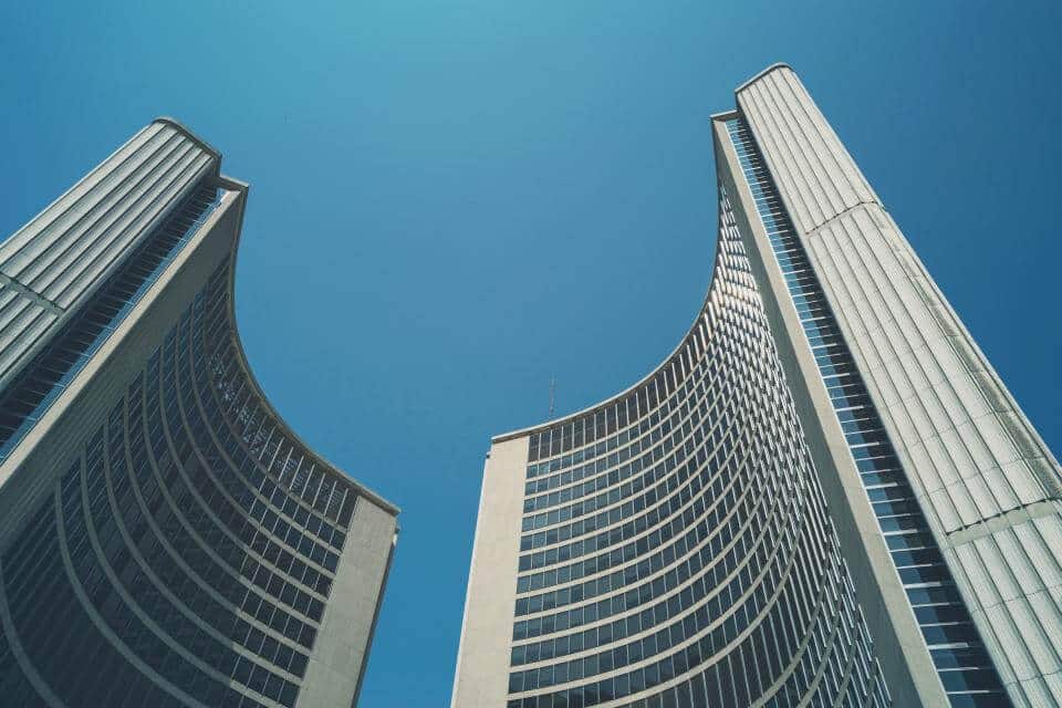 Two modern, curved skyscrapers against a clear blue sky, creating an open, symmetrical architectural space.