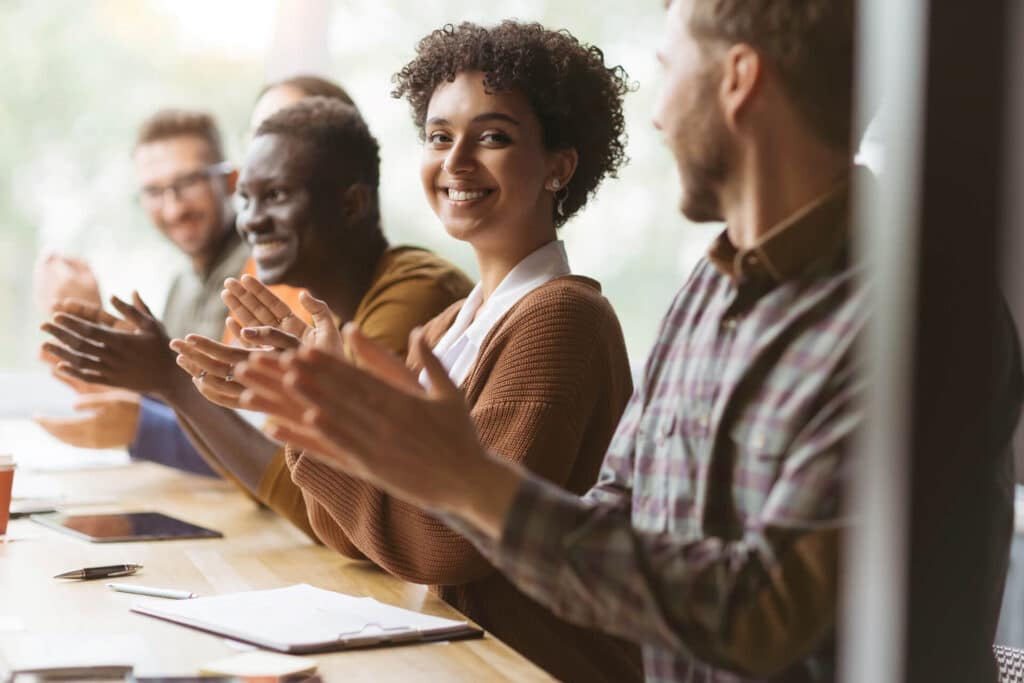 A diverse group of people sitting at a table, smiling and clapping.