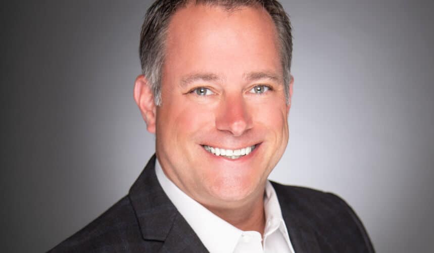 Smiling man in a suit poses against a gray background.