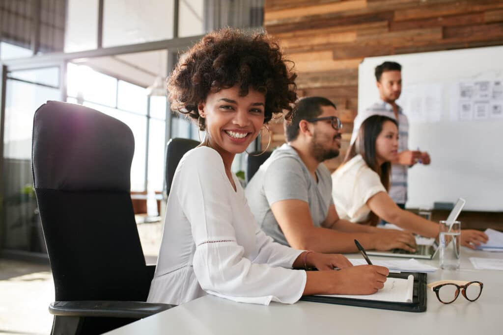 Smiling woman at a conference table with colleagues working in a modern office.