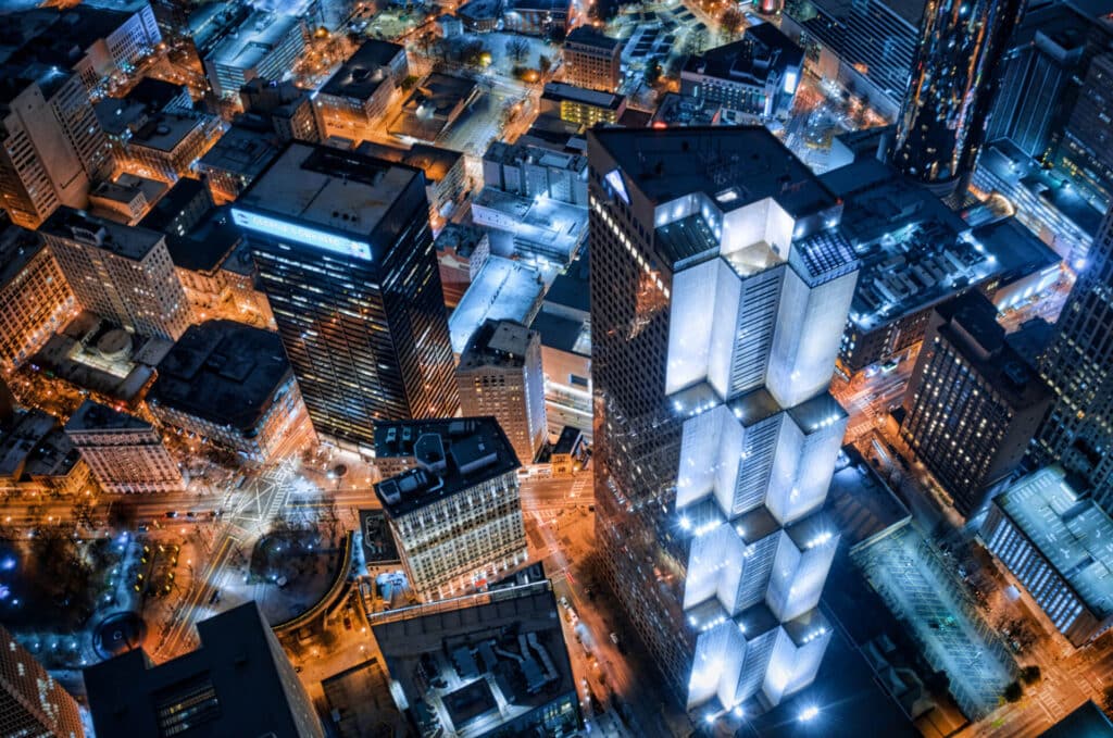 Aerial view of a city at night with tall, illuminated skyscrapers and a network of brightly lit streets.
