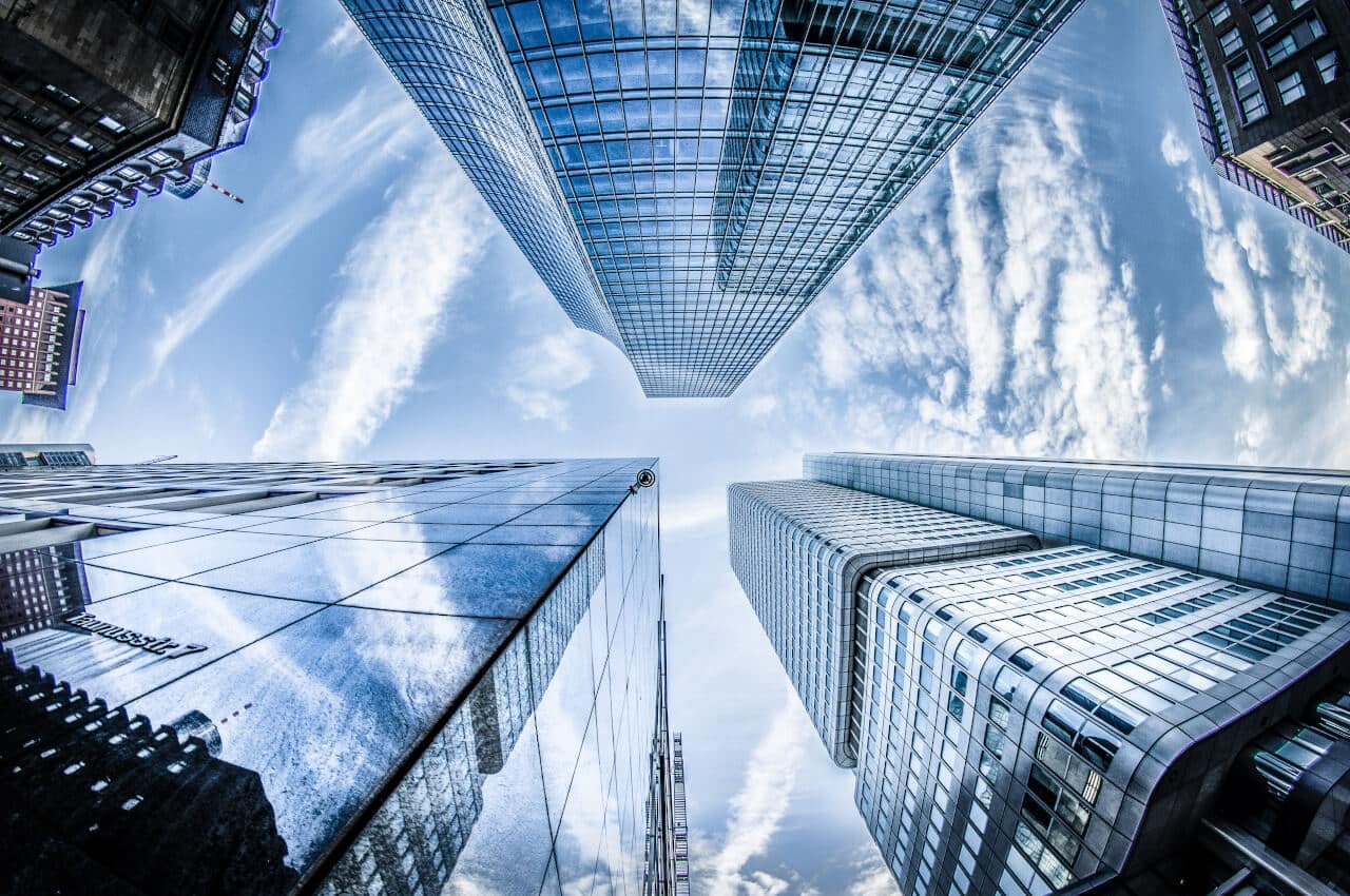 Fisheye view of skyscrapers against a cloudy blue sky, reflecting clouds on their glass surfaces.