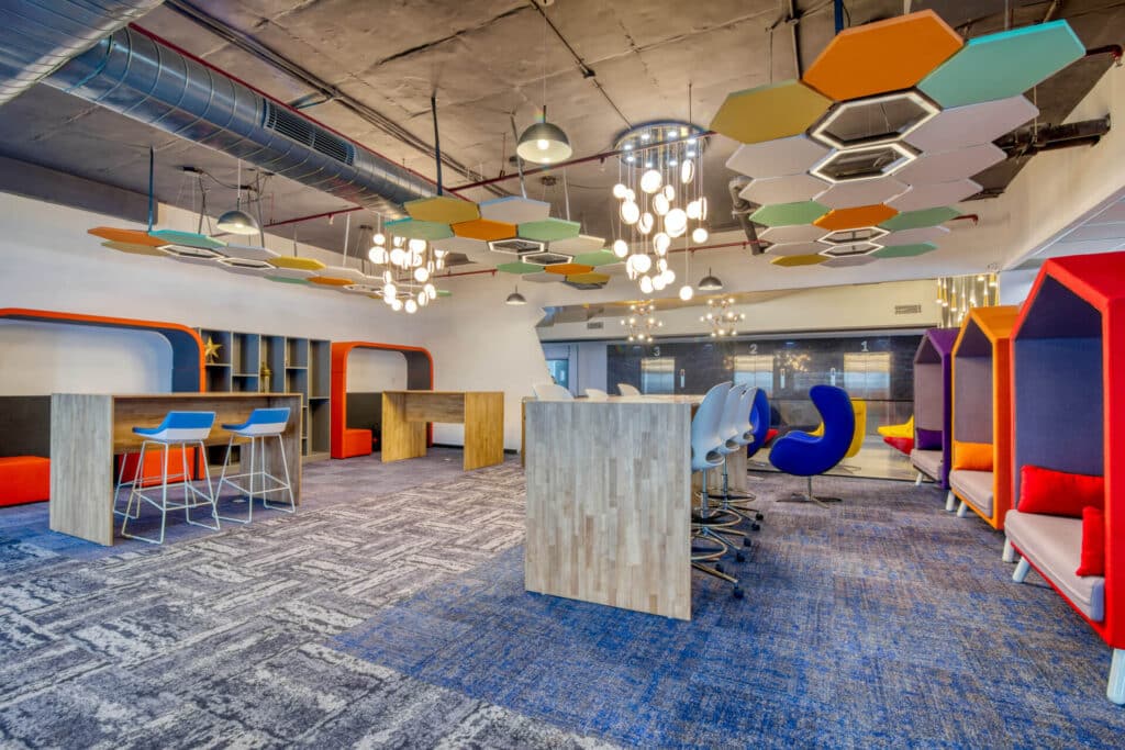 Modern office space with colorful geometric ceiling panels, bar stools, and seating pods.