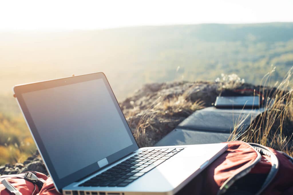 Open laptop on a backpack atop a rocky cliff with a blurred landscape in the background.