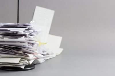 A large stack of disorganized papers on a desk with a plain gray background.