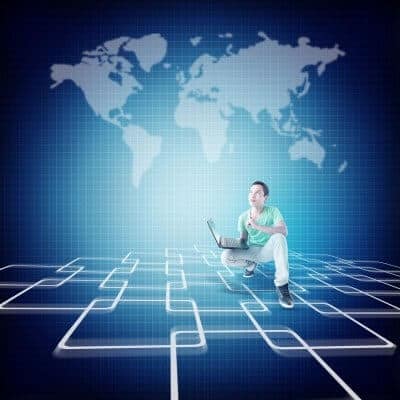 Person crouching with a laptop on a grid-like floor with a world map in the background.