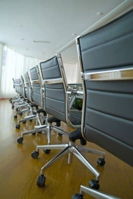 Row of empty gray office chairs on wheels around a conference table on a wooden floor.