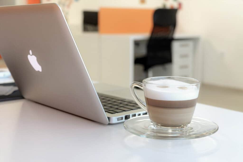 A glass cup of coffee sits beside an open laptop on a desk in a modern office setting.