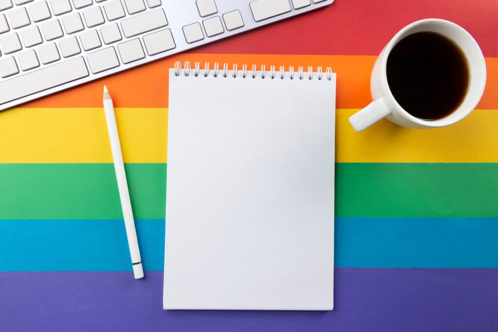 A notebook, pencil, keyboard, and coffee cup on a rainbow-striped background.