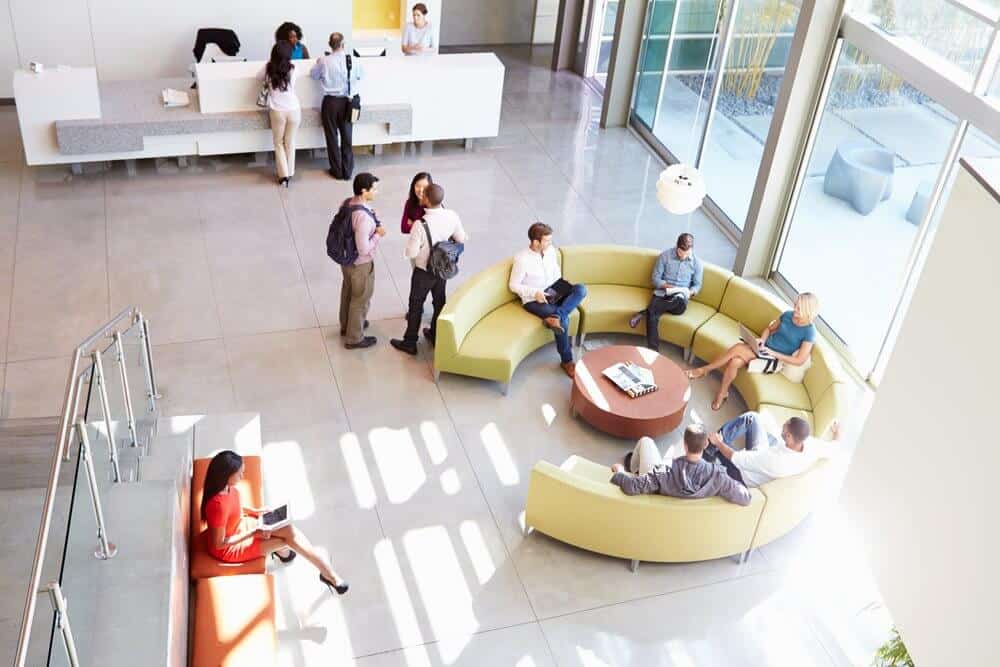 People socializing and working in a bright, modern lobby with circular seating and a reception desk.