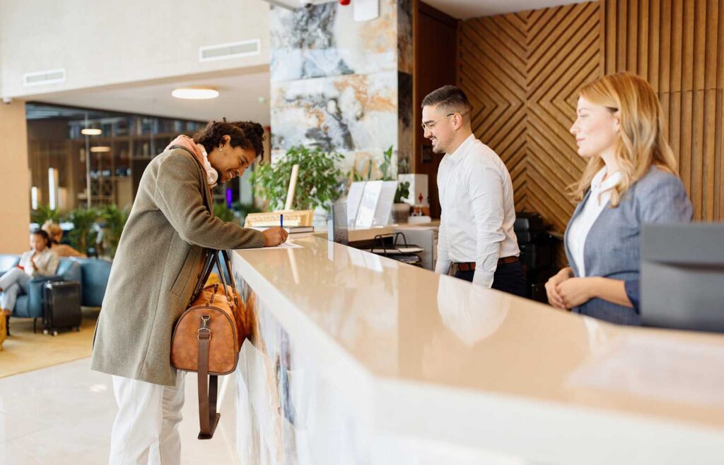 Person checking in at a hotel reception desk, with two staff members assisting.