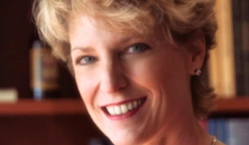 Smiling woman with short blonde hair in a blurred indoor setting.