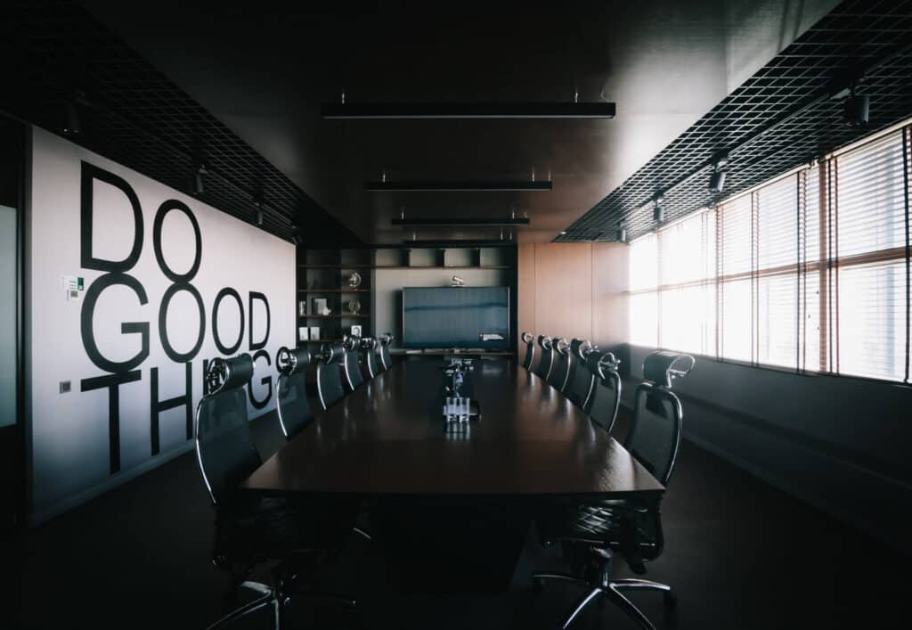 Dark conference room with a long table, office chairs, and wall text saying "DO GOOD THINGS.
