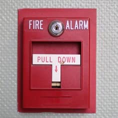 Red fire alarm pull station on a textured wall surface.