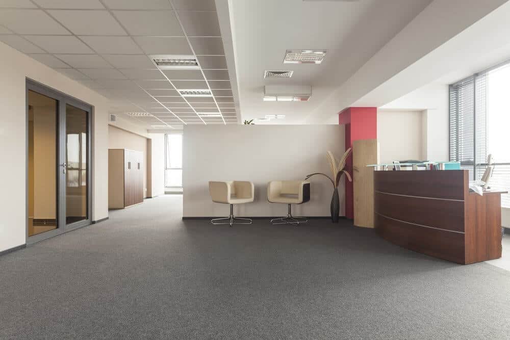 Modern office lobby with two beige chairs, a wooden reception desk, and large windows letting in natural light.