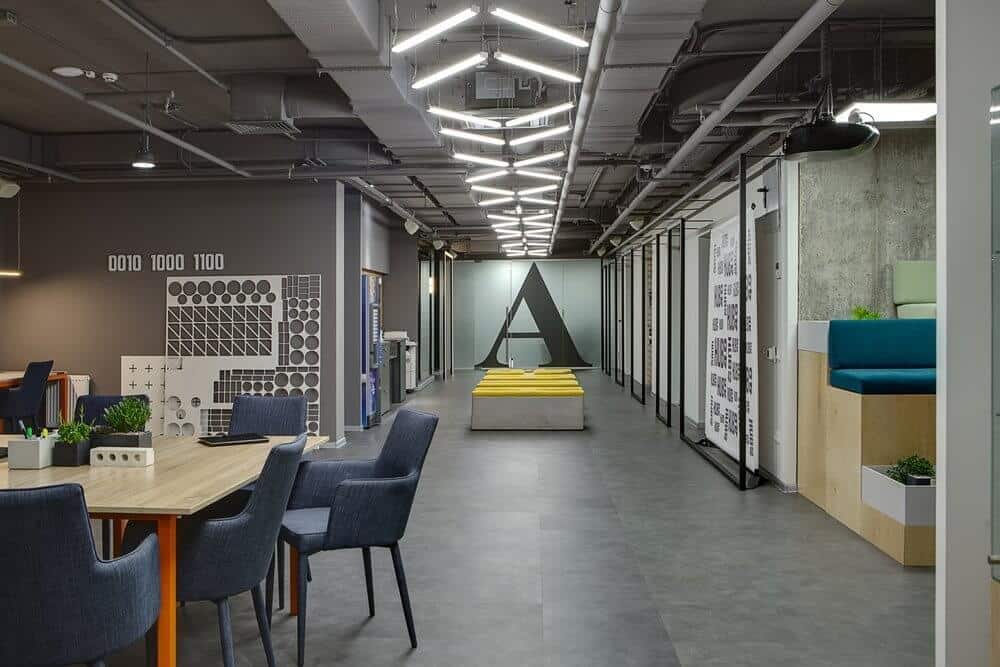 Modern office interior with geometric lighting, gray tones, seating areas, and a large letter "A" on the wall.