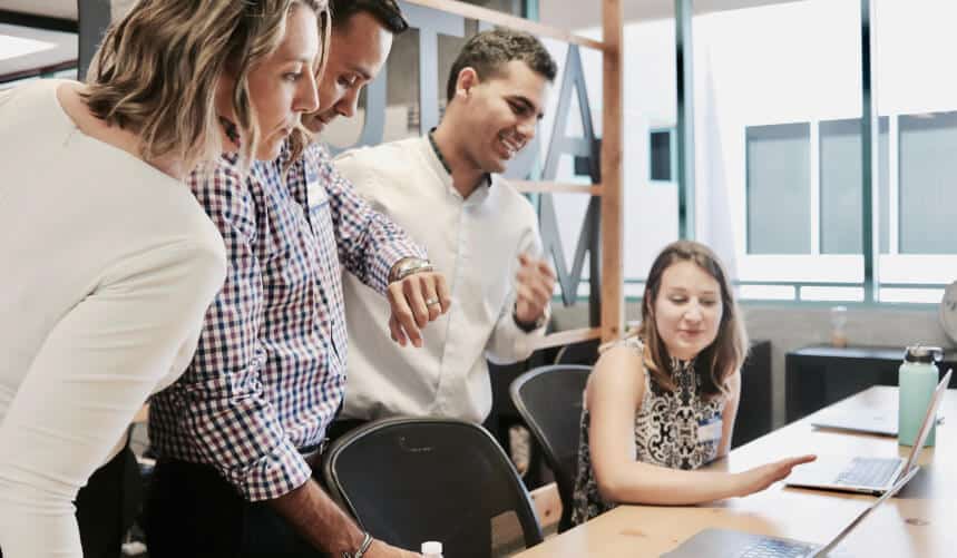 Four people gathered around a laptop in an office, discussing and collaborating.