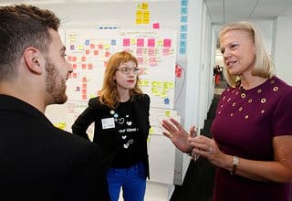 Three people discussing in front of a wall covered in colorful sticky notes and charts.