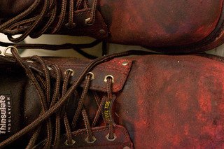 Close-up of scuffed brown leather boots with red stains and dark brown laces.