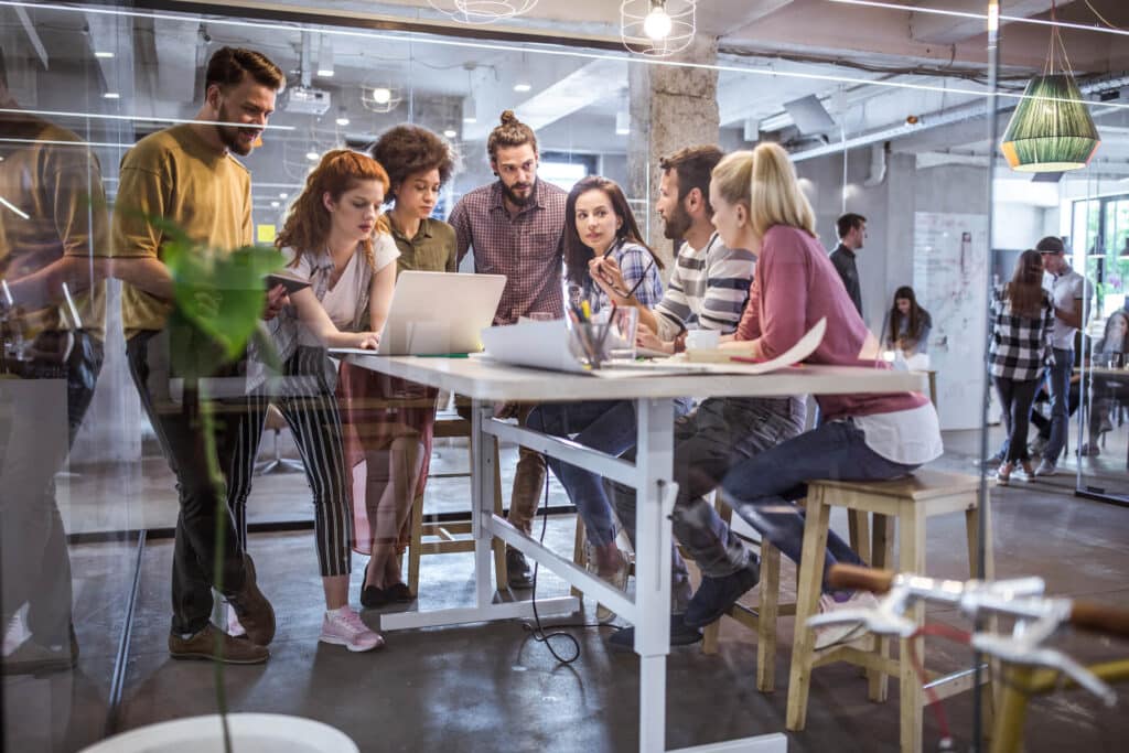 A group of people collaborating around a high table in a modern office space with glass walls.