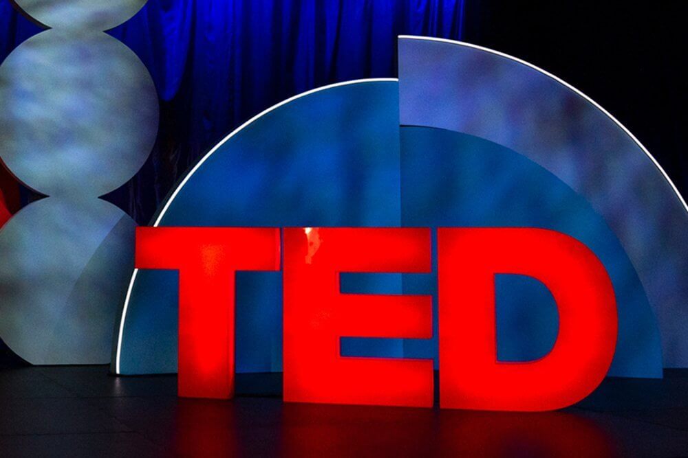 Red "TED" letters in front of abstract blue and white background shapes.