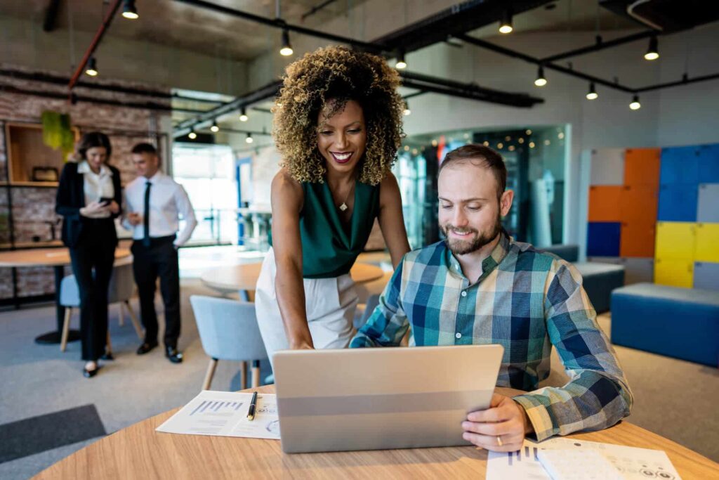 Man and woman huddled around a laptop in a modern office space