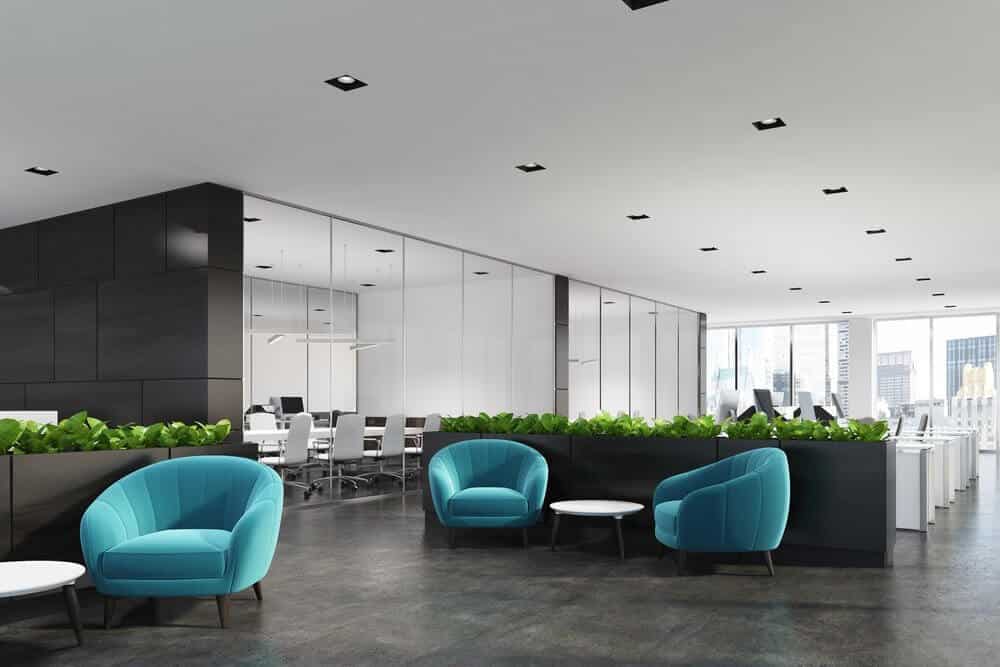 Modern office with teal chairs, white tables, green plants, and glass-walled meeting room; city view in the background.