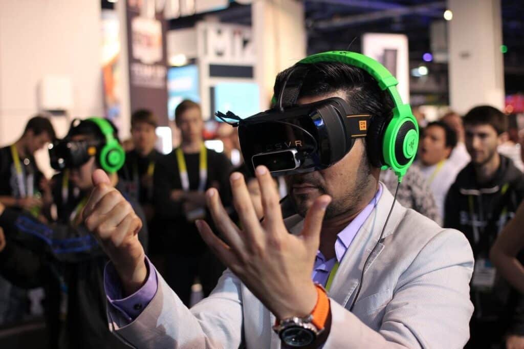 Person using a VR headset and green headphones in a crowded tech event.