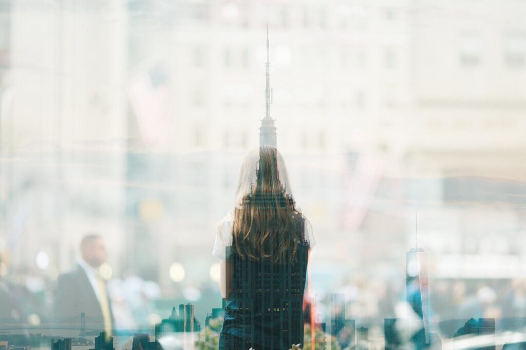 A woman with long hair faces a cityscape overlay, including the Empire State Building, in a dreamy double exposure.