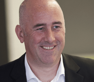 A smiling bald man in a suit, looking slightly to the side.